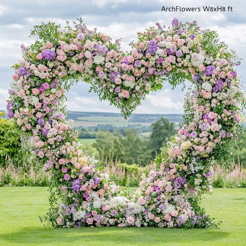 May include: A heart-shaped floral arch, approximately 8 feet wide and 8 feet high, composed of pink, purple, and white flowers. The arch is set on a green lawn with a scenic background of trees and a cloudy sky. Text on the image reads "ArchFlowers W8xH8 ft."