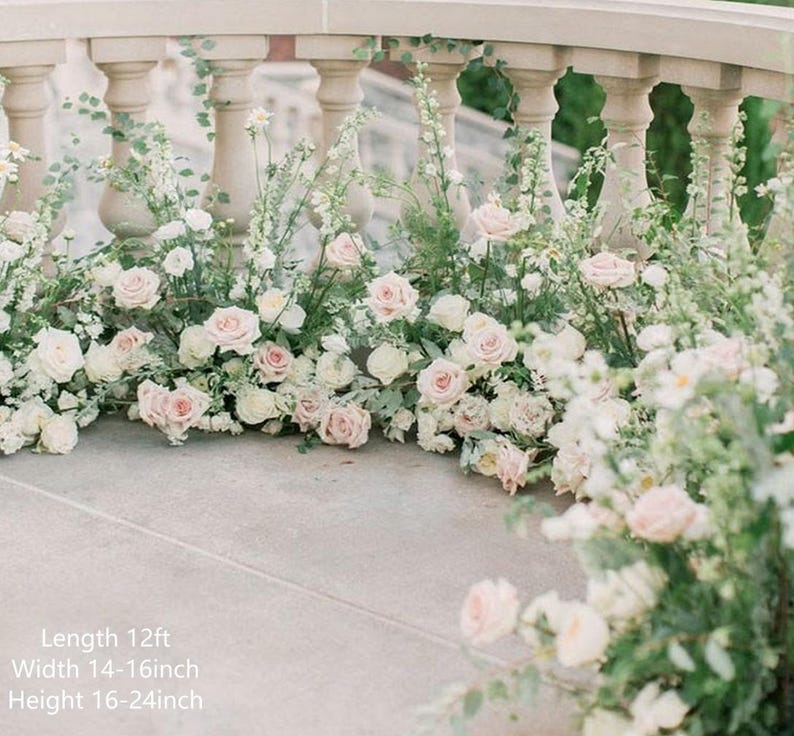 Op de afbeelding: Een bruiloftceremonie achtergrond gemaakt van witte en roze bloemen, groen en wijnstokken. De bloemstukken zijn 3,66 meter lang, 35,56 tot 40,64 centimeter breed en 40,64 tot 61 centimeter hoog.