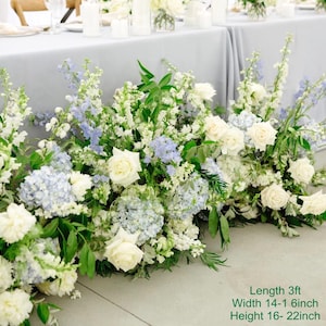 Puede incluir: Un pasillo de ceremonia de boda decorado con flores blancas y azules. Las flores est&aacute;n dispuestas en cascada, creando un ambiente rom&aacute;ntico y elegante. Las flores incluyen rosas blancas, hortensias azules y lisianthus blancos. El pasillo tiene aproximadamente 3 pies de largo, 14-16 pulgadas de ancho y 16-22 pulgadas de alto.