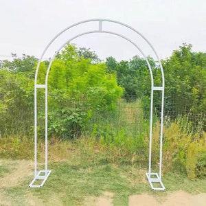 May include: White metal archway for a wedding or other event. The archway is freestanding and has a simple design.