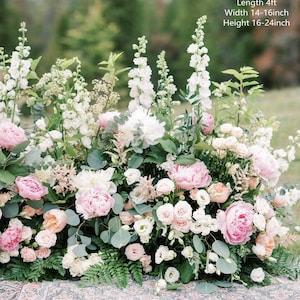 Op de afbeelding: Een bloemstuk met witte en roze bloemen, waaronder pioenen, rozen en groen. De opstelling is ongeveer 1,2 meter lang, 35-40 centimeter breed en 40-60 centimeter hoog.