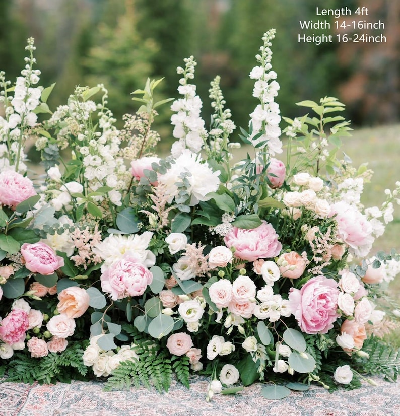 Op de afbeelding: Een bloemstuk met witte en roze bloemen, waaronder pioenen, rozen en groen. De opstelling is ongeveer 1,2 meter lang, 35-40 centimeter breed en 40-60 centimeter hoog.