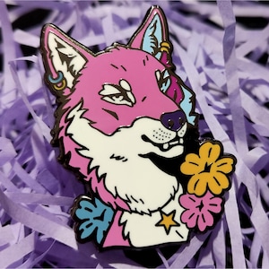 May include: A pink and white fox enamel pin with black outlines, featuring a floral bouquet. The fox has blue and yellow accents, and is wearing earrings. The pin is set against a background of purple paper.