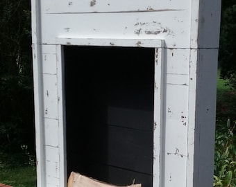 May include: White painted wooden fireplace mantel with a black painted interior and a hearth with two pieces of firewood. The mantel is distressed and has a rustic look.