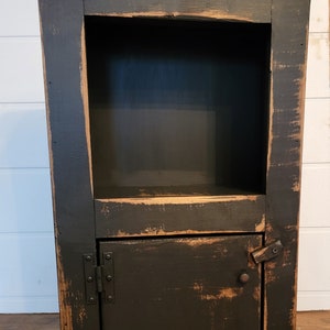May include: A black wooden cabinet with a distressed finish. It has a single door with a metal hinge and a small shelf inside. The cabinet is about 30 inches tall.