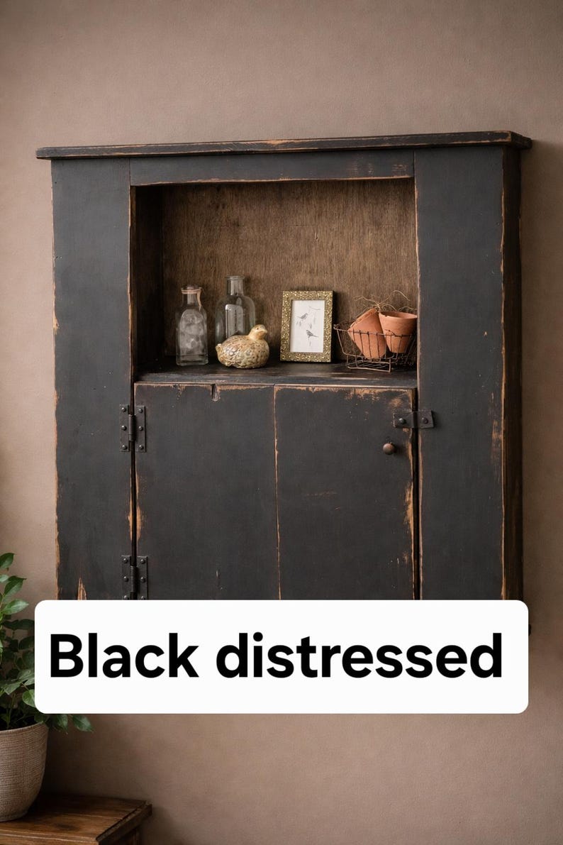 May include: Black distressed cabinet with a rustic design. The cabinet has a distressed finish and features a small shelf with decorative items, including bottles, a bird figurine, and a framed picture. The cabinet has a door with a latch.