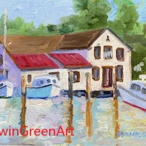 May include: A painting depicting a waterfront scene with a white building featuring a red roof and three boats moored in front. The building has a wooden veranda and a wooden balustrade. The boats are all white with blue trim. The water is a light blue colour and the sky is a light blue colour. The painting is signed "Edwin GreenArt".