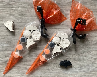 May include: Two orange and white Halloween-themed paint-your-own kits. Each kit includes a ghost, bat, skull, and other Halloween-themed shapes, along with paint pots.