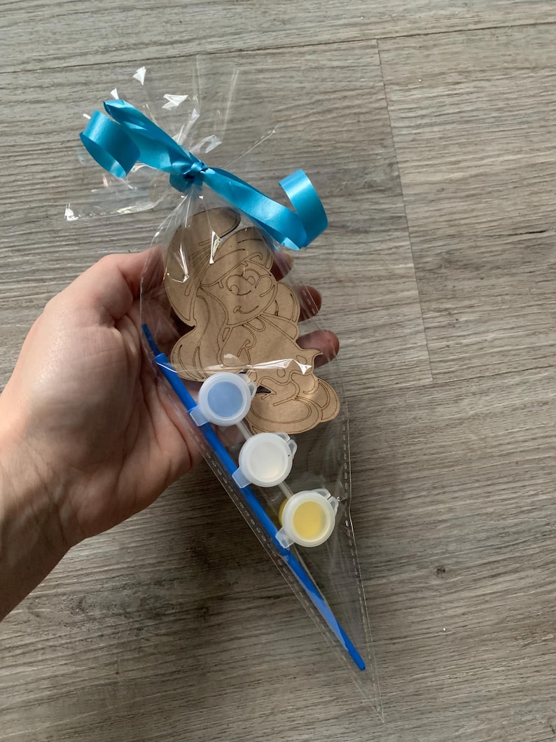 Pu&ograve; includere: Un sacchetto di cellophane trasparente legato con un nastro blu contiene una figura di legno dei Puffi, vasetti di vernice e un pennello. Il Puffo &egrave; non verniciato e pronto per essere colorato. I vasetti di vernice sono blu, bianchi e gialli.