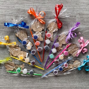 Pu&ograve; includere: Un set di dieci ornamenti in legno di personaggi da dipingere, ognuno confezionato con un piccolo pennello e un set di barattoli di vernice. I personaggi sono tutti cani dei cartoni animati con diverse espressioni e pose. Gli ornamenti sono avvolti in cellophane trasparente e legati con nastri colorati.