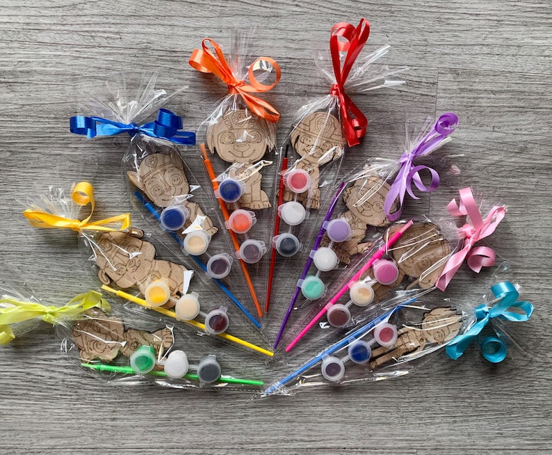 Pu&ograve; includere: Un set di dieci ornamenti in legno di personaggi da dipingere, ognuno confezionato con un piccolo pennello e un set di barattoli di vernice. I personaggi sono tutti cani dei cartoni animati con diverse espressioni e pose. Gli ornamenti sono avvolti in cellophane trasparente e legati con nastri colorati.