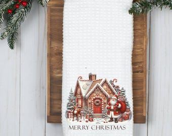 May include: White kitchen towel featuring a gingerbread house and Santa Claus design. The house is decorated with candy canes and the text "Merry Christmas" is printed below the image.