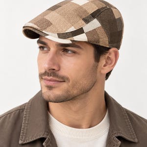 May include: A flat cap featuring a multi-tonal plaid pattern in shades of brown, tan, cream, and dark chocolate. The hat has a structured, rounded crown and a short, stiff brim that curves slightly downward at the front, creating a classic silhouette.