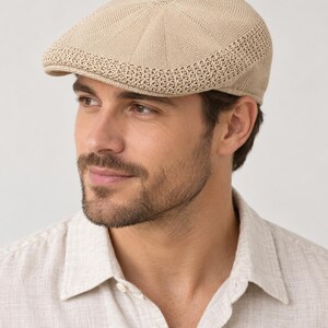 May include: A beige flat cap featuring a knit construction with a textured, open-weave band along the lower edge. The cap has a structured crown with radial stitching patterns and a short, stiff brim extending from the front of the headwear.