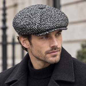 May include: A newsboy cap featuring a textured, salt-and-pepper tweed pattern in shades of black, white, and gray. The cap has a rounded, multi-paneled crown with a small fabric-covered button at the top center and a short, stiffened brim.