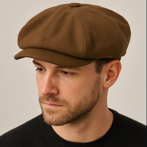 May include: A brown newsboy cap with a rounded crown and a small, stiff brim. The cap is made of a soft, textured fabric and has a classic, vintage style. The cap is a solid, warm brown color.