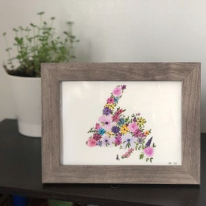 Peut inclure: Une peinture à l'aquarelle encadrée représentant un arrangement floral en forme de province. Les fleurs sont dans des tons de rose, de violet, de jaune et de bleu. Le cadre est de couleur marron clair. La peinture est signée "AL '20".