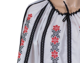 May include: White embroidered blouse with black and red floral designs. The blouse has a gathered neckline and long sleeves.