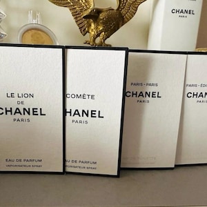 Op de afbeelding: Vier witte Chanel parfumdozen met zwarte tekst. De dozen zijn gelabeld met "Le Lion de Chanel", "Comète", en twee dozen met "Chanel Paris". De dozen zijn voor Eau de Parfum en Eau de Toilette.