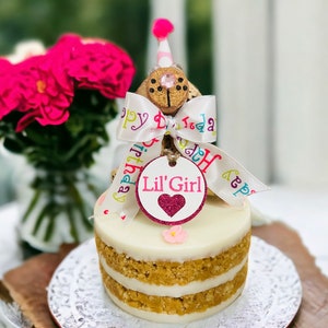 Peanut Butter Dog Cake with pink flowers and keepsake girl birthday dog made out of corks with a party hat, personalized dog tag, birthday ribbon and birthday hat.