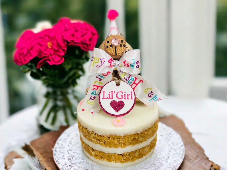 Peanut Butter Dog Cake with pink flowers and keepsake girl birthday dog made out of corks with a party hat, personalized dog tag, birthday ribbon and birthday hat.
