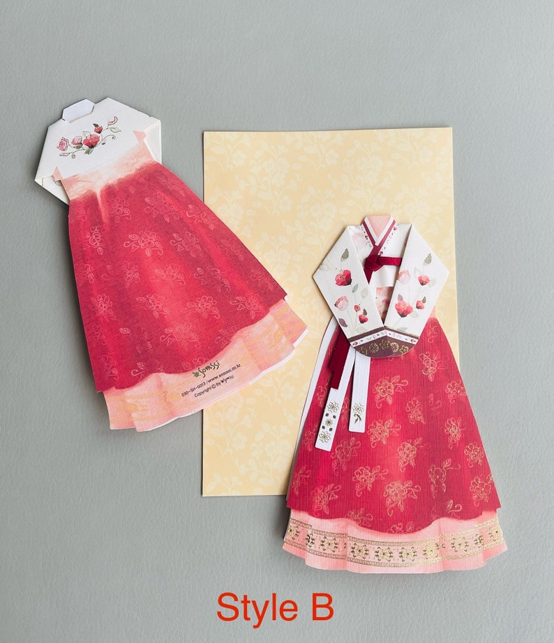 May include: Two red and white paper cut-out dresses in the style of traditional Korean Hanbok. The dresses are decorated with floral patterns and gold accents. The text "Style B" is printed below the dresses.