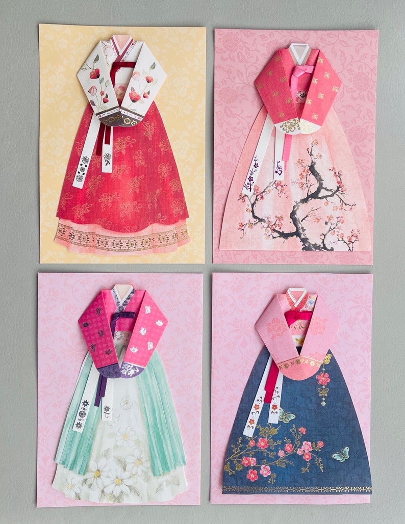 May include: Four cards with origami paper cutouts of traditional Korean hanbok dresses. Each card features a different color and pattern, including red, pink, green, and blue. The dresses are decorated with floral and butterfly motifs.