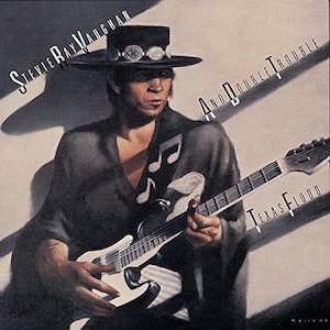 May include: Album cover art featuring Stevie Ray Vaughan and Double Trouble. Vaughan is depicted wearing a black hat and playing a white and black electric guitar. The album title "Texas Flood" is displayed in white text.