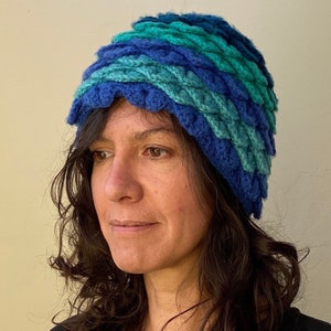 May include: A woman wearing a blue and green crocheted hat with a scalloped edge.