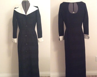 May include: A long black dress with a white collar and cuffs. The dress has a button-up front and a fitted waist.