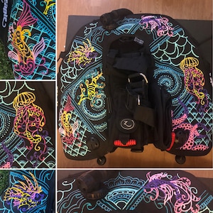 Puede incluir: Un BCD de buceo negro con un diseño colorido y estampado. El patrón presenta medusas, peces y otras criaturas marinas en tonos de rosa, azul, amarillo y verde.