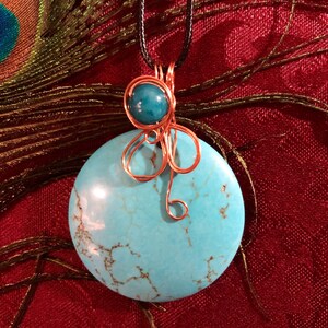 May include: A turquoise pendant necklace with a copper wire design. The pendant is a round, flat stone with a marbled pattern. The necklace is on a black cord.