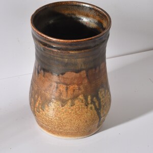 May include: A brown and black ceramic vase with a textured surface. The vase has a wide mouth and a narrow base.