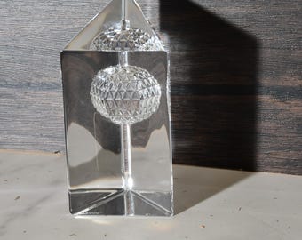 May include: A clear glass paperweight with a geometric design. The paperweight is shaped like a sphere and is sitting on a clear glass base.
