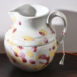 May include: A white ceramic pitcher with a speckled design in shades of yellow and red. The pitcher has a rounded body and a handle.