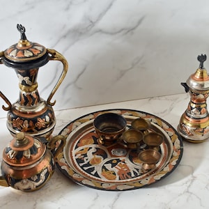 May include: A set of ornate copper and brass serving pieces, including a teapot, two pitchers, and a tray with six small cups. The tray is decorated with intricate floral and geometric designs.
