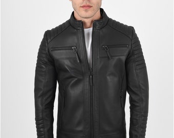 Puede incluir: Chaqueta de cuero negra con cuello alzado, cierre de cremallera y detalles acolchados en hombros y brazos. Cuenta con dos bolsillos en el pecho con cremallera y dos bolsillos laterales. La chaqueta se lleva sobre una camiseta blanca y vaqueros oscuros.