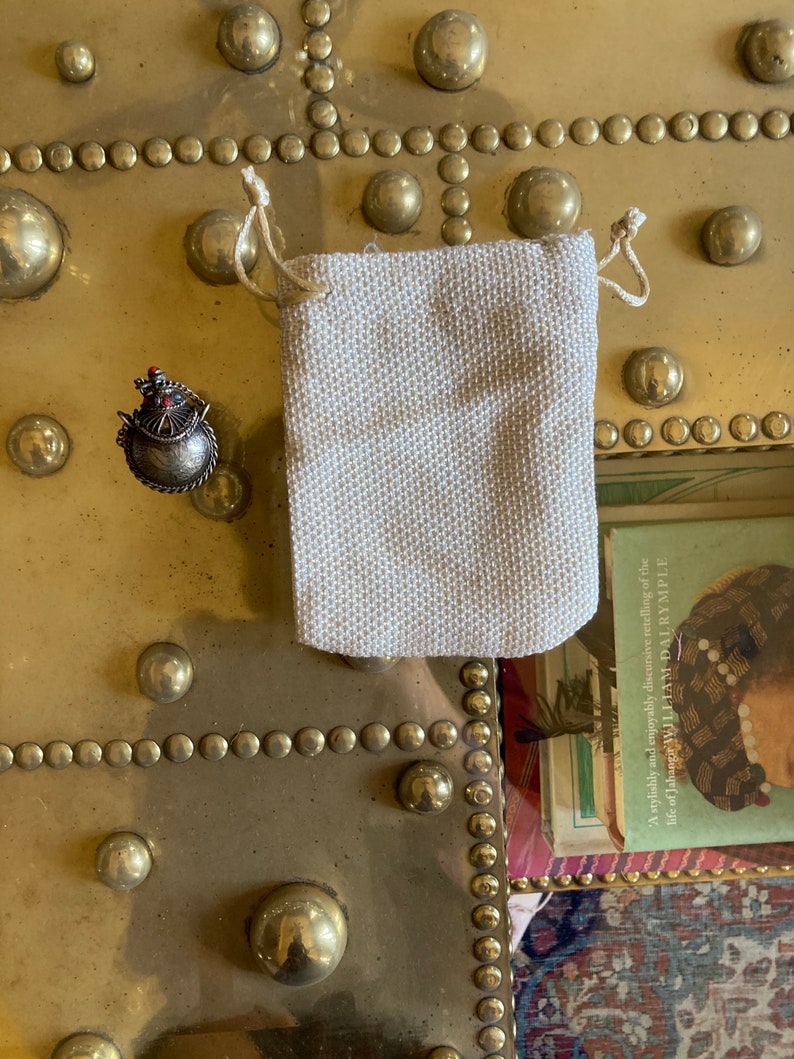 May include: A small, ornate, silver-colored, jeweled, bird-shaped pendant in a small, off-white, drawstring pouch.