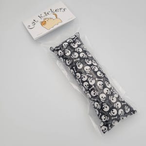 May include: A black cat toy with a white skull and crossbones pattern. The toy is packaged in a clear plastic bag with a white label that says "Cat Kickers".