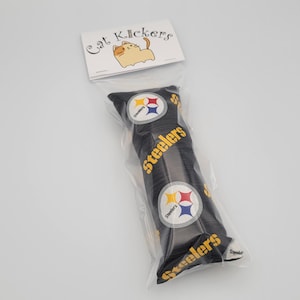 May include: A black and yellow catnip toy shaped like a pillow with the Pittsburgh Steelers logo and the word "Steelers" repeated on the fabric. The toy is packaged in a clear plastic bag with a white label that says "Cat Kickers" and has a cartoon cat on it.