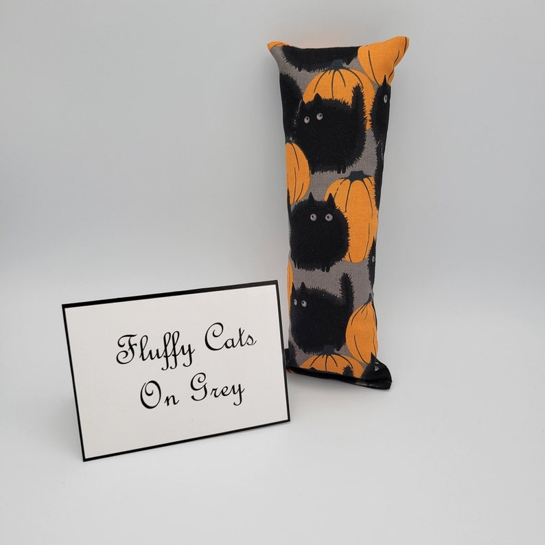 May include: A long, rectangular pillow with a gray background and a repeating pattern of black cats and orange pumpkins. The pillow has the text "Fluffy Cats On Grey" on a white card in front of it.