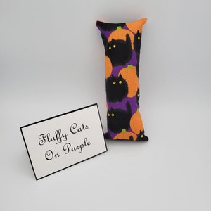 May include: A purple and orange cat-themed pillow with the text "Fluffy Cats On Purple" on a white card.