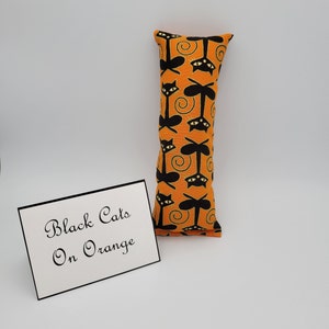 May include: Orange cat-shaped pillow with black cats on it. The pillow has the text "Black Cats On Orange" on a white card next to it.