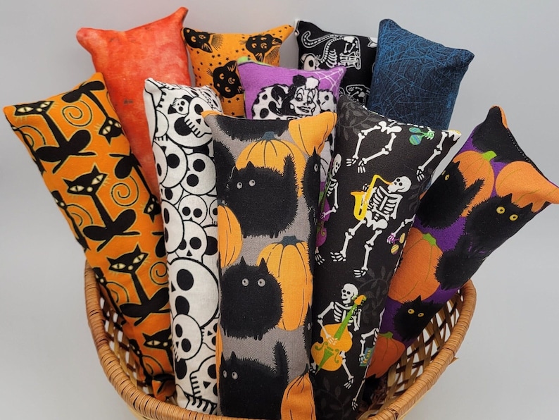 May include: A basket filled with Halloween-themed catnip toys. The toys are made of fabric and feature various designs, including skulls, pumpkins, and cats.