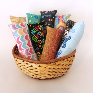 May include: A wicker basket filled with colorful fabric cat toys. The toys have various patterns, including a birthday cake, a tie-dye design, and a nautical theme.