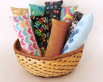 May include: A wicker basket filled with colorful fabric cat toys. The toys have various patterns, including a birthday cake, a tie-dye design, and a nautical theme.