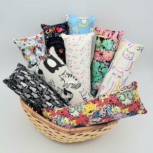 May include: A wicker basket filled with ten colorful catnip toys. The toys are made of fabric and have different cat-themed patterns, including cats, hearts, and stars.