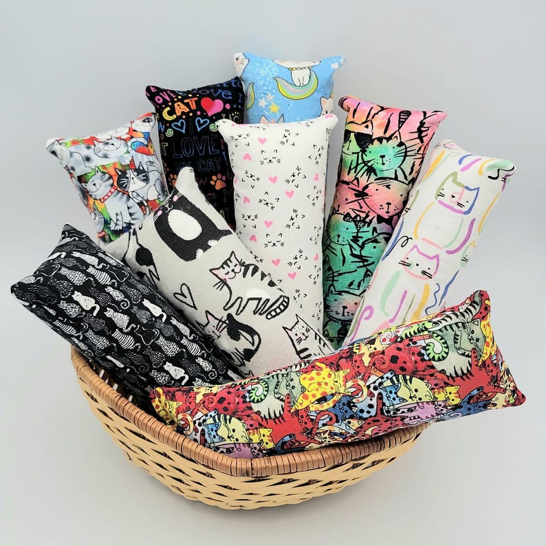 May include: A wicker basket filled with ten colorful catnip toys. The toys are made of fabric and have different cat-themed patterns, including cats, hearts, and stars.