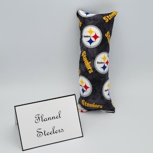 May include: A black and gray flannel pillow with the Pittsburgh Steelers logo repeated on the fabric. The pillow is rectangular and has a white tag that says "Flannel Steelers".