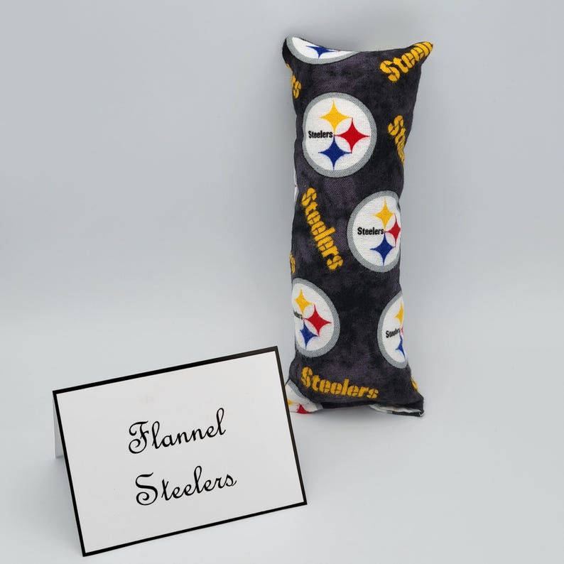 May include: A black and gray flannel pillow with the Pittsburgh Steelers logo repeated on the fabric. The pillow is rectangular and has a white tag that says "Flannel Steelers".